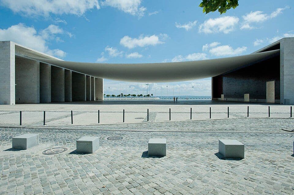 Pavilhão de Portugal, com uma pala de betão curva suspensa entre dois pórticos e o rio ao fundo
