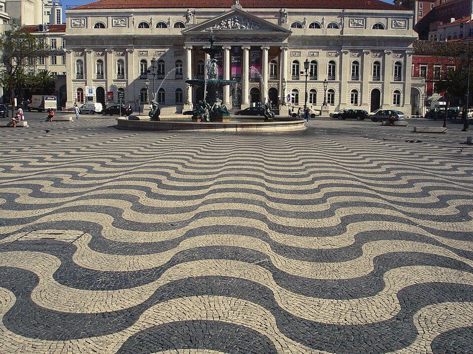 Praça do Rossio com calçada em ondas pretas e brancas, a fonte e o Teatro D. Maria II ao fundo