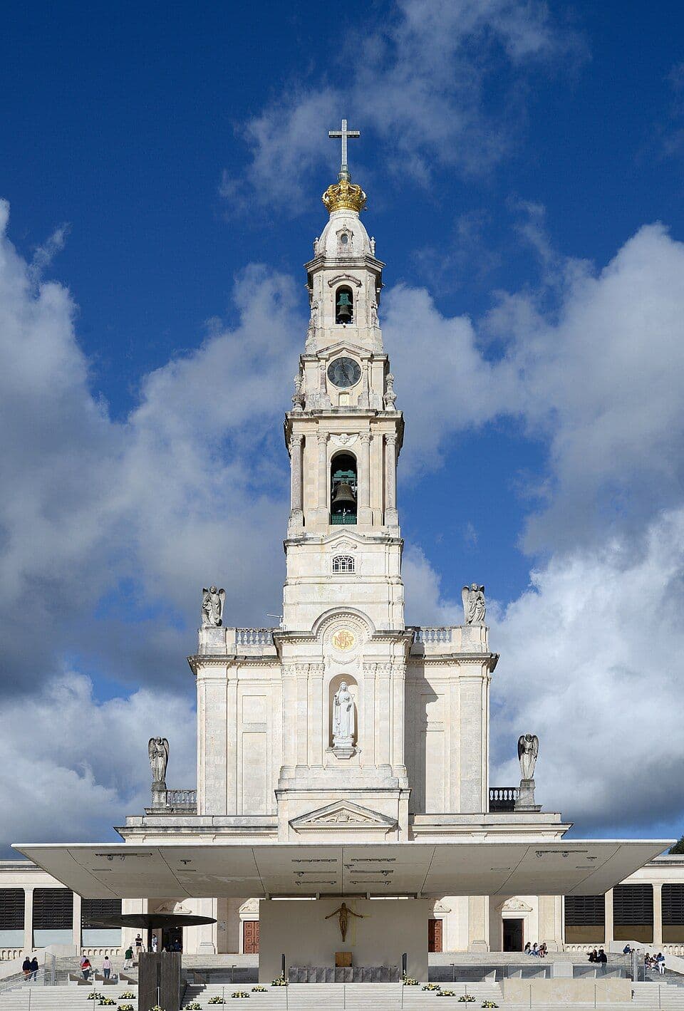 Torre da Basílica de Nossa Senhora do Rosário, em Fátima, com a coroa dourada no topo e céu azul com nuvens