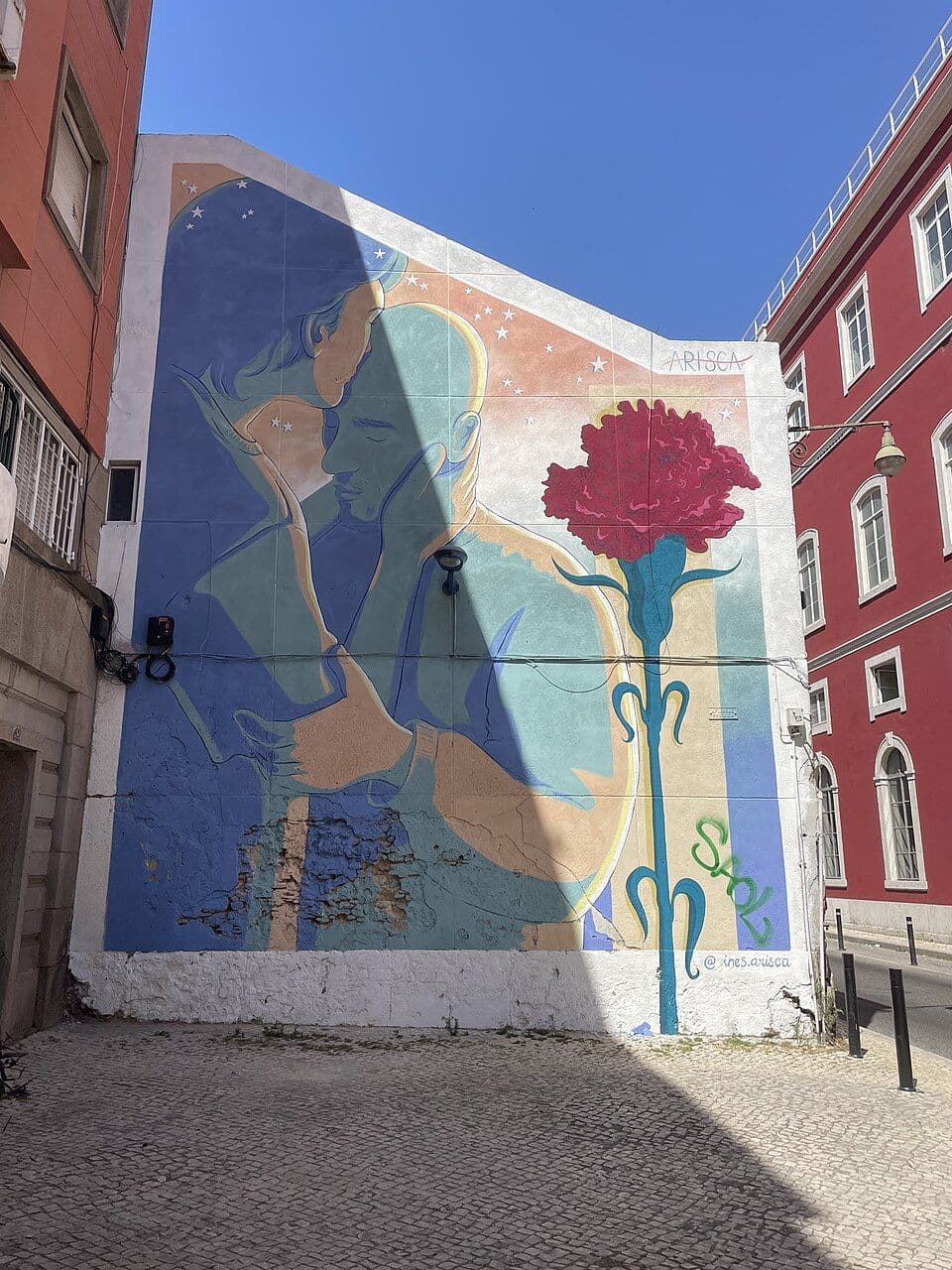 Mural numa empena de Lisboa com um casal abraçado e um grande cravo vermelho