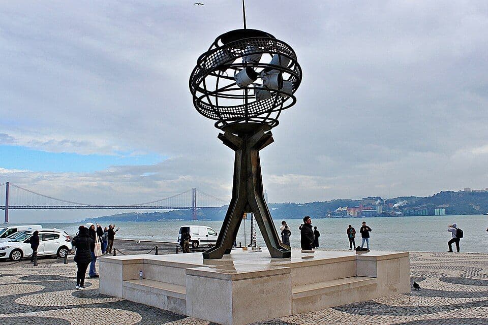 Escultura de uma esfera armilar de metal na margem do Tejo, em Belém, com a Ponte 25 de Abril ao fundo